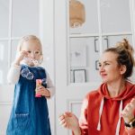 A joyful moment of a mother and daughter playing with bubbles indoors.