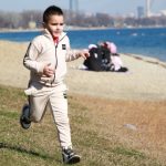Young boy in a tracksuit runs energetically by the waterfront, embodying the joy of a sunny day outdoors.